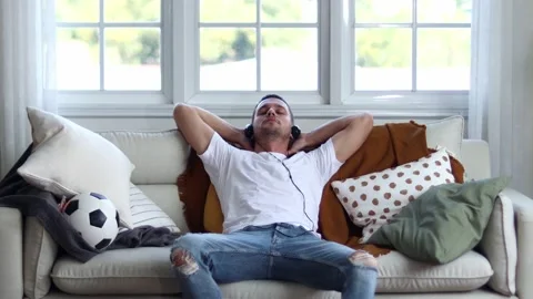 A man in Headphones Using Smartphone Sitting On sofa Indoor. Stock Footage 163087998