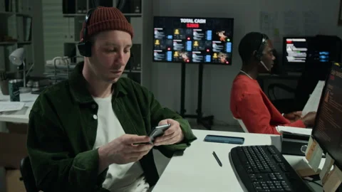 Man with Headset Checking Smartphone While Working in Scam Office at Night Stock Footage 346709510