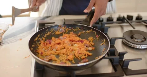 Man hearing sizzling on kitchen stove using spatula in pan stirring carrots and Stock Footage 342018712