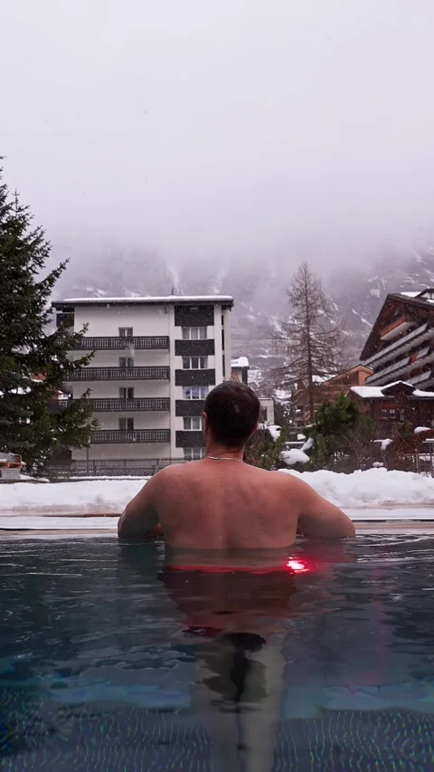 Man at heated infinity pool in Zermatt facing chalet buildings Stock Footage 331968111