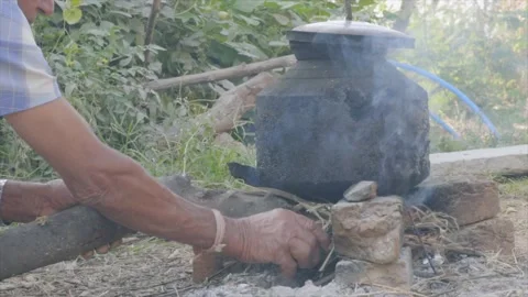 A man heating water over a fire in a village Stock Footage 228197015
