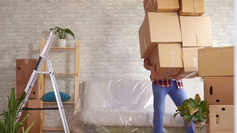 Man with heavy boxes in his hands loses his balance and falls on the sofa slow Vídeos de archivo 105285907
