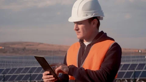 A man in a helmet engineer on the background of a solar power plant holding a Stock Footage 97164050