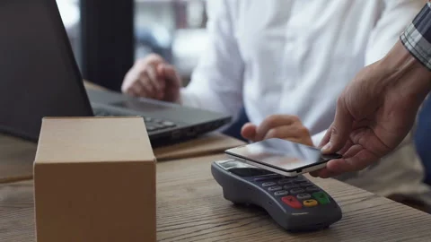 The man with the help of a payment terminal and the phone pays the parcel 库存影片 98951261