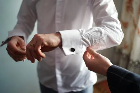 A man is helped to put on the cufflink of a white shirt. Stock Photos