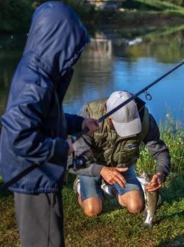 Man helping boy to remove hook from caught trout fish at lake during vacation Stock Photos