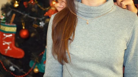 Man helping his girlfriend to try on a golden necklace by christmas tree. Stock Footage 100297103
