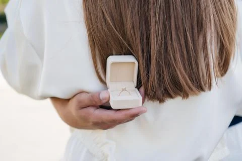 Man hiding a small box with a diamond engagement ring behind a woman's back, 库存照片