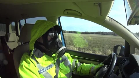 Man with high visibility jacket and gasmask, driving a car through countryside Stock Footage 146012123