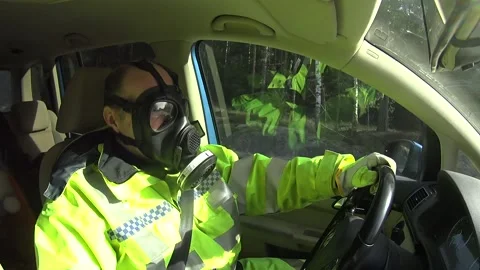 Man in a high visibility jacket and gasmask, driving a car through countryside Stock Footage 146012137