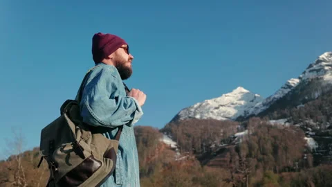 Man hiker with backpack standing on top of the mountain, looking at the snow Video stock 231698485
