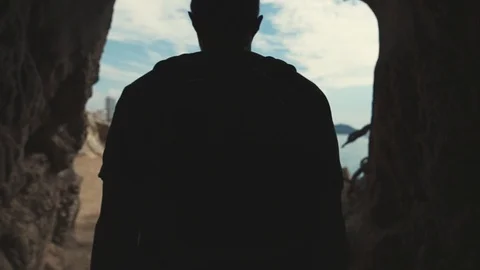 Man hiker is going out from dark cave on sunny area with seascape and cityscape Stock Footage 100113151