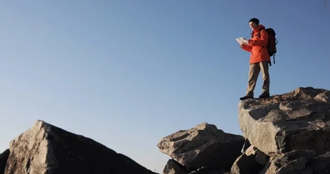 Man hiker is looking at the map in mountains checking the route. Standing on big Stock Footage 106086104