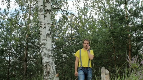 Man hiker walking through the forest and talking on the phone. Yellow T-shirt Stock Footage 66269279