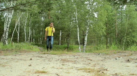 Man hiker walking through the forest and talking on the phone. Yellow T-shirt Stock Footage 66270454