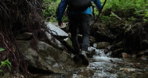 A man hiker walks through a mountain stream in the forest Stock Footage 243722720