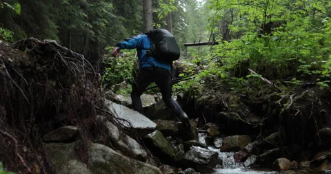 A man hiker walks through a mountain stream in the forest Stock Footage 243722758