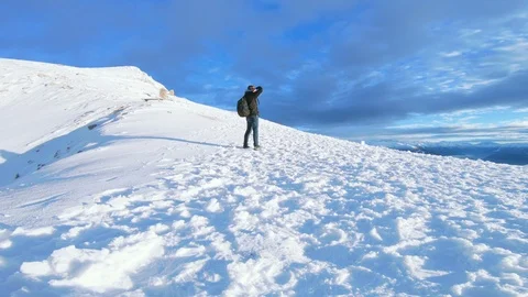 Man hikes with backpack on a steep snow covered mountain and enjoys the view Stock Footage 100053006