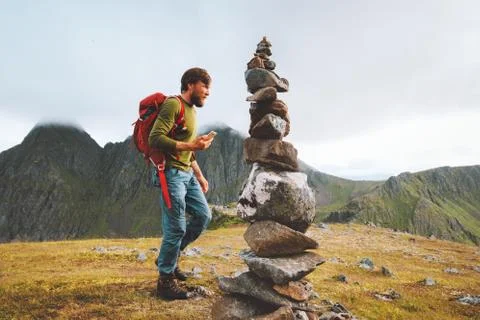 Man hiking with backpack using smartphone for navigation rock cairn marking r Stock Photos