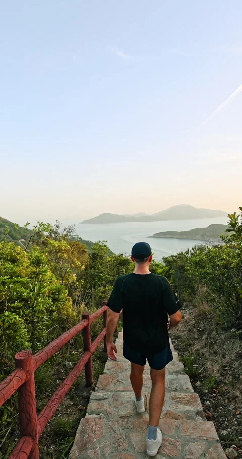 Man Hiking Down Stone Stairs Overlooking Scenic Coastal Bay Video stock 332304016