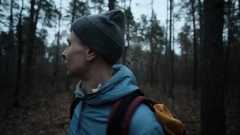 A man in hiking gear wanders through a dense forest, looking around with Stock Footage 300958030