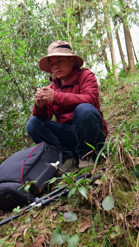 A man hiking in mountain forest squats on the ground to eat chocolate 動画素材 329550460