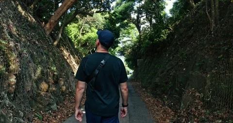Man Hiking on Narrow Road Between Steep Forested Embankments Stock Footage 332609396