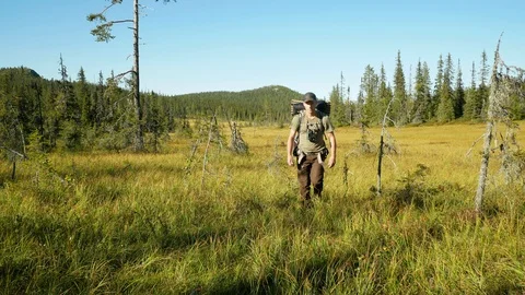 Man hiking over an open field with backpack Stock Footage 98301750