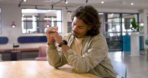 Man in his 20s smiling in office-lounge, sitting at round table, checking watch Stock Footage 341393532