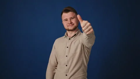 Man in his 30s on blue background giving thumbs up then thumbs down, changing Stock Footage 265651605