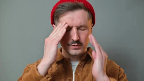 A man in his 30s is expressing discomfort by holding his head and rubbing his Видео 337643167