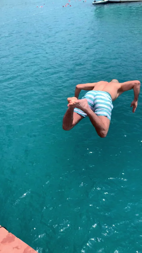 A man in his 30s jumping off the top of a boat into clear blue water Stock Footage 200251071