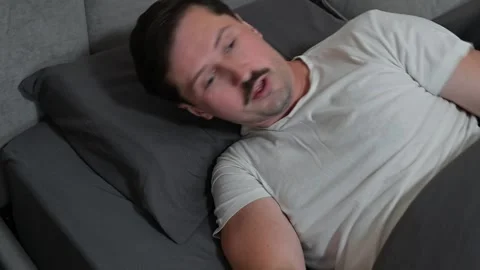 A man in his 30s lies in bed and wakes up, stretching his arms before getting up Stock Footage 344527684