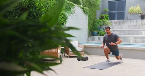 Man in his 30s stepping onto exercise mat, jogging, doing reverse lunges on Stock Footage 341736701