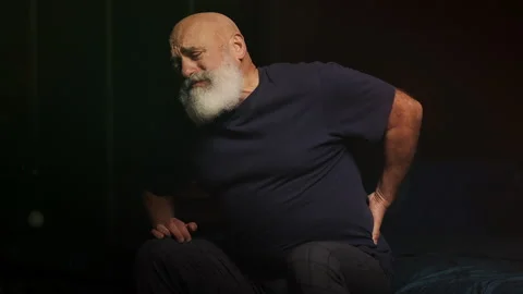 Man in his 50s feels lower back pain while sitting on bed, radiculitis Stock Footage 346714377