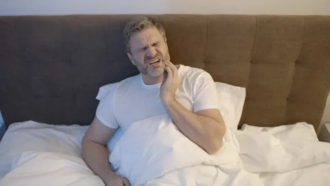 Man in his 50s lying in bed and touching his jaw, suffering from toothache Stock-Footage 154592069