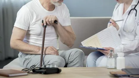 Man in his 50s sitting on sofa and talking with doctor, healthcare and illness Stock Photos