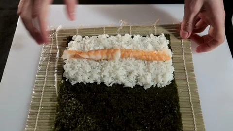 A man with his bare hands makes a roll with a shrimp. On the table is a sheet 스톡 동영상 86933105