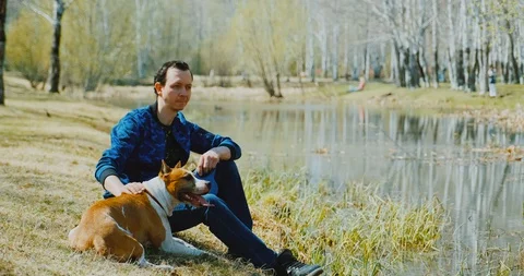 Man with his dog outdoors, sit beside river in park alone. Pensive calm look. Stock Footage 130152053