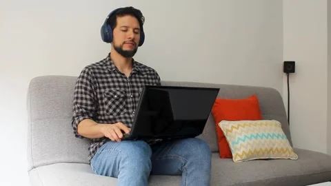 Man with his eyes closed sitting on a couch listening music on a headset Stock Footage 340583414