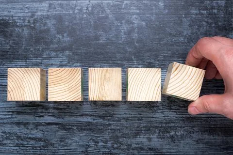 Man with his hand puts empty wooden cube to rest in row on table. Stock Photos
