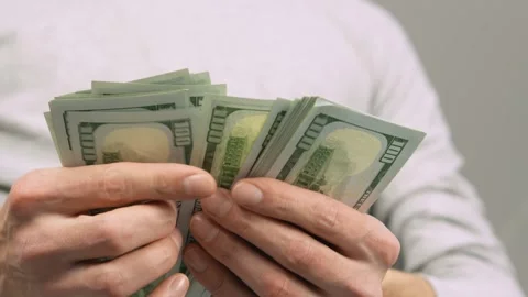 A man in his hands holds a pack of hundred-dollar bills and counts them. This Stock Footage 257898593