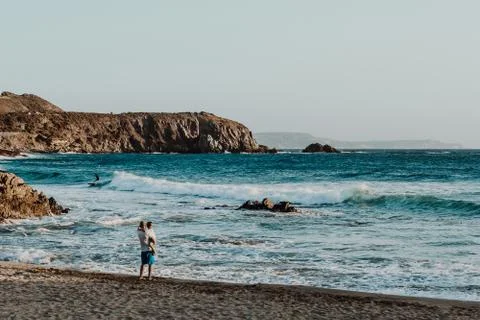A man with his son at the beach looking surfers Stock Photos