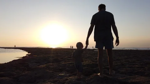A man with his two-year-old son are on the beach towards the setting sun Stock Footage 111849669