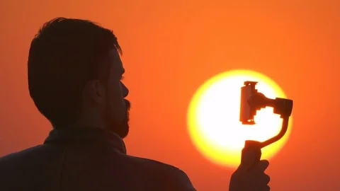 The man hold camera stabilizer with a phone on the sunset background Stock Footage 80749189