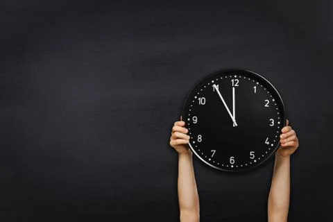 Man hold round office clock on black chalkboard background Stock Photos
