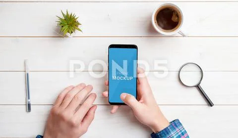Man hold smart phone mockup. Top view, flat lay composition with white wooden de PSD-Vorlage