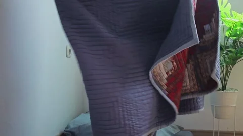 Man holding up and neatly folding heavy quilted blanket in bright room Vidéo 341994785