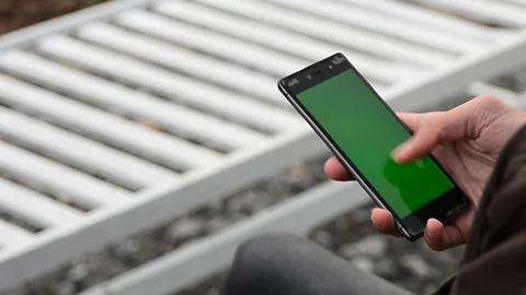 Man holding and using modern looking smartphone outdoors with green screen Stock Footage 103246888