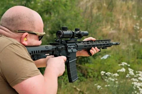 A man is holding an automatic weapon. a man looks into the sight of a militar 写真素材